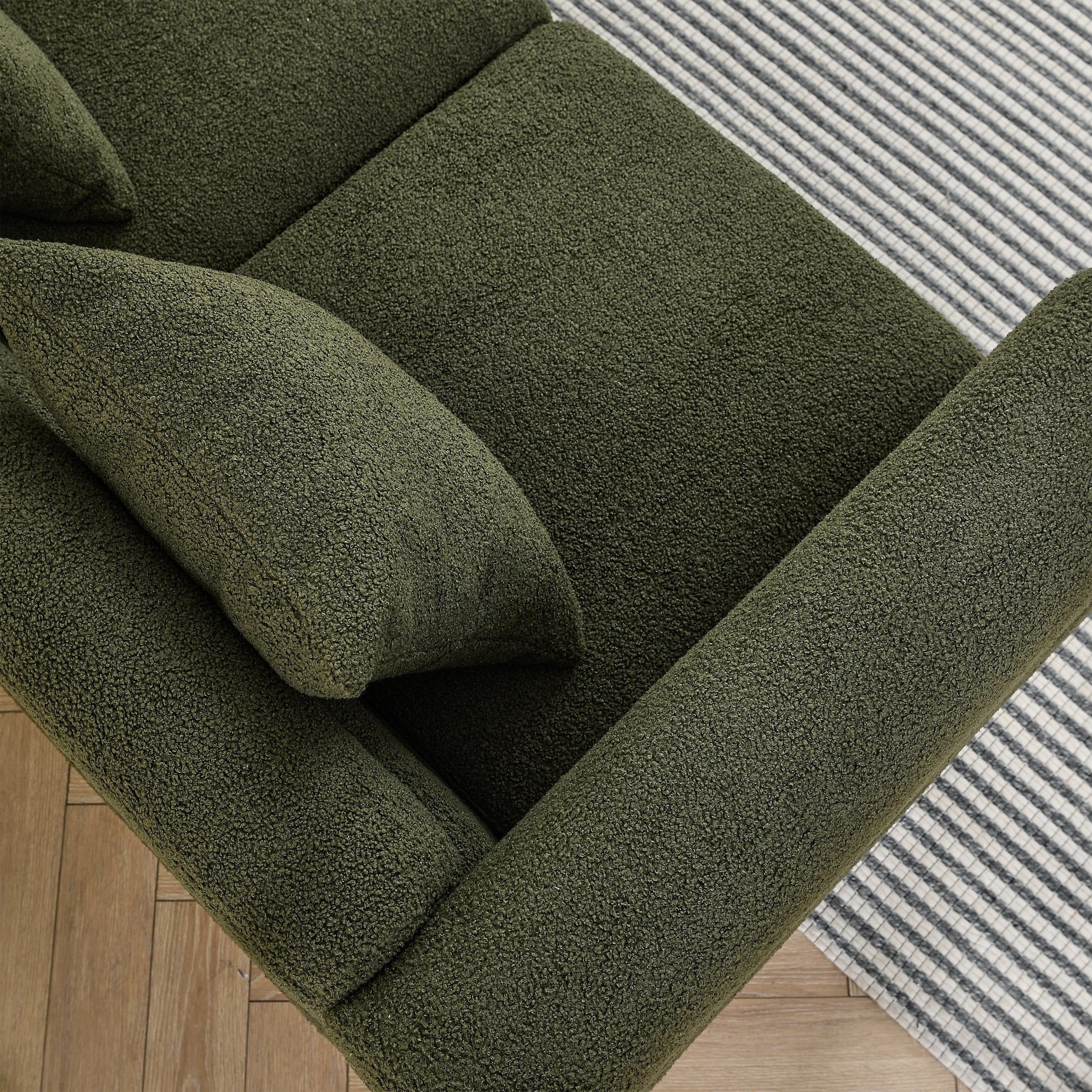 Green textured sofa with cushions on a wooden floor and striped rug