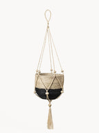 Woven plant hanger with black base and beige top, featuring tassels on a white background.