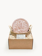 Decorative pink ceramic coaster with bird design in a cardboard box on a white background