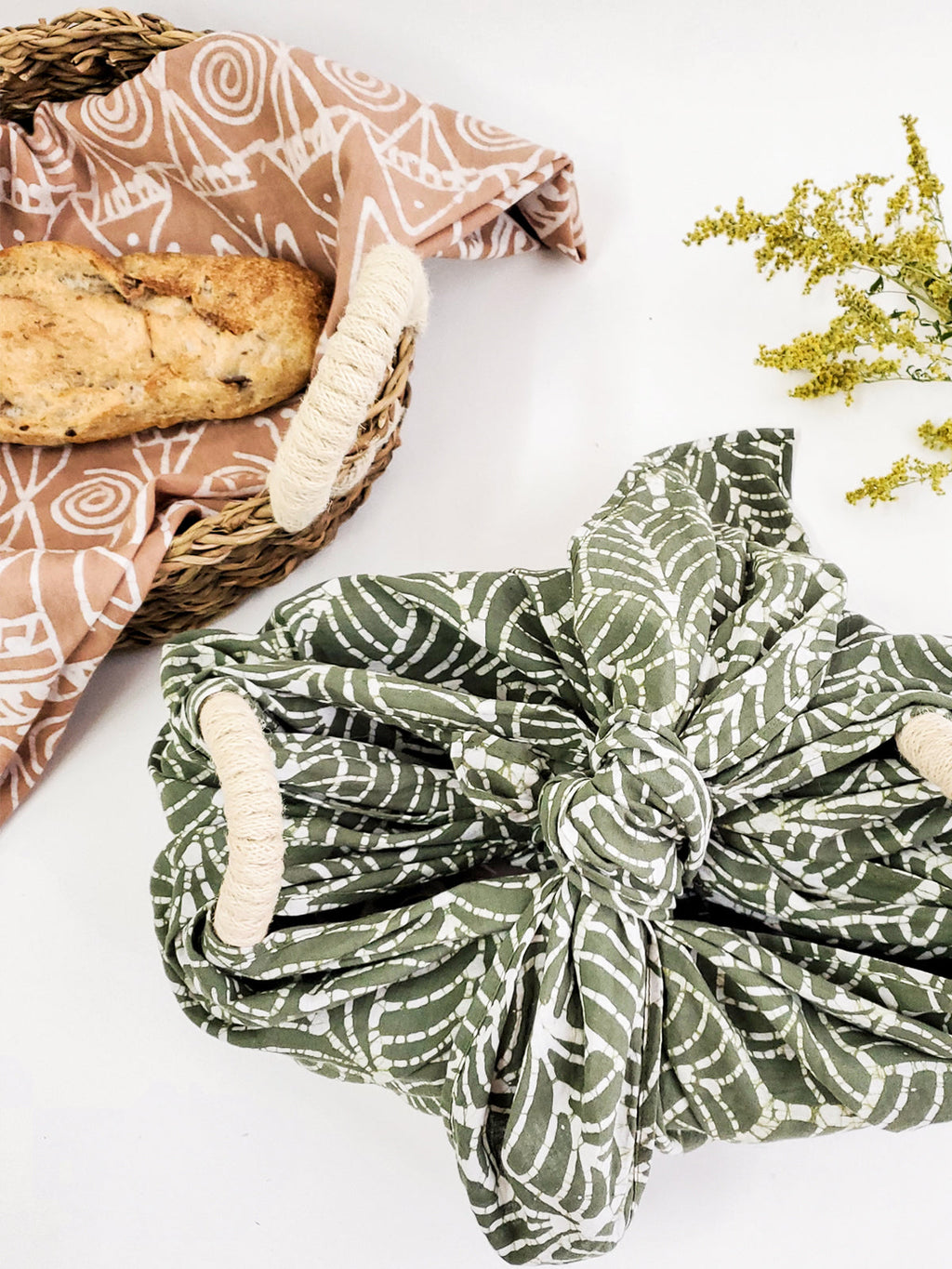 Green patterned fabric wrapped around a basket with bread on a white background