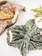 Green patterned fabric wrapped around a basket with bread on a white background