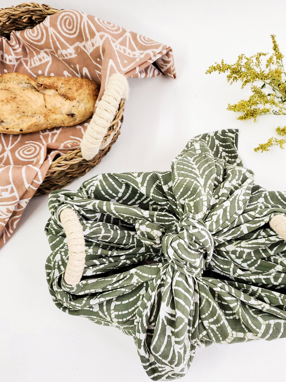 Green patterned fabric wrapped around a basket with bread on a white background