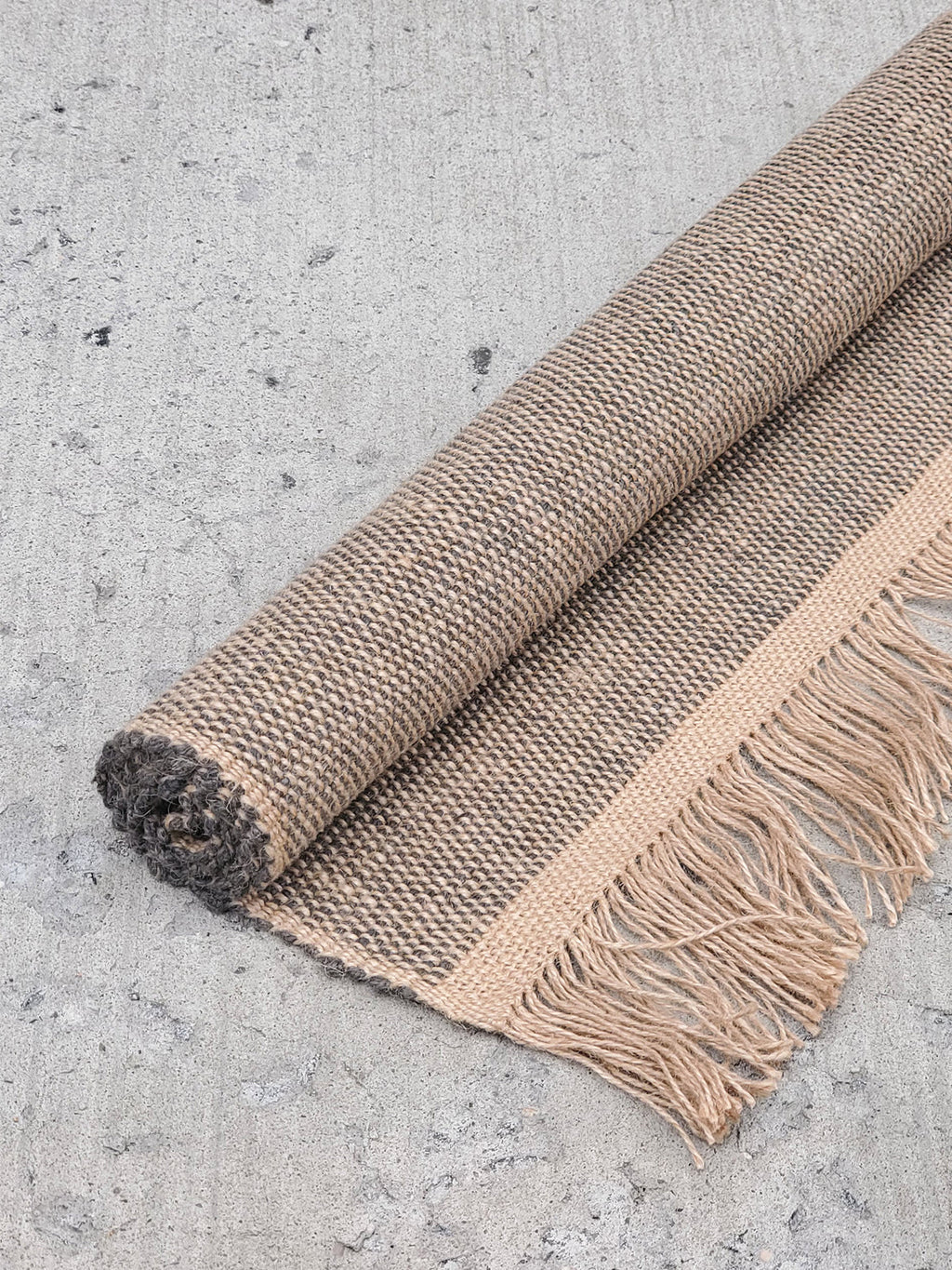 Brown woven rug with fringes on a concrete floor