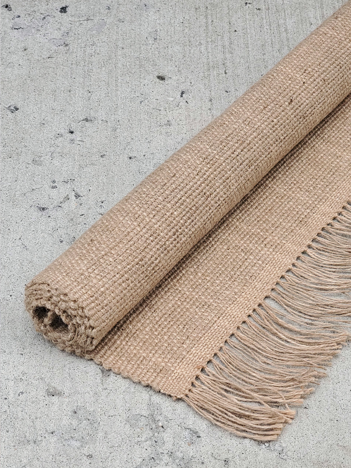 Beige woven rug with fringes on a concrete floor
