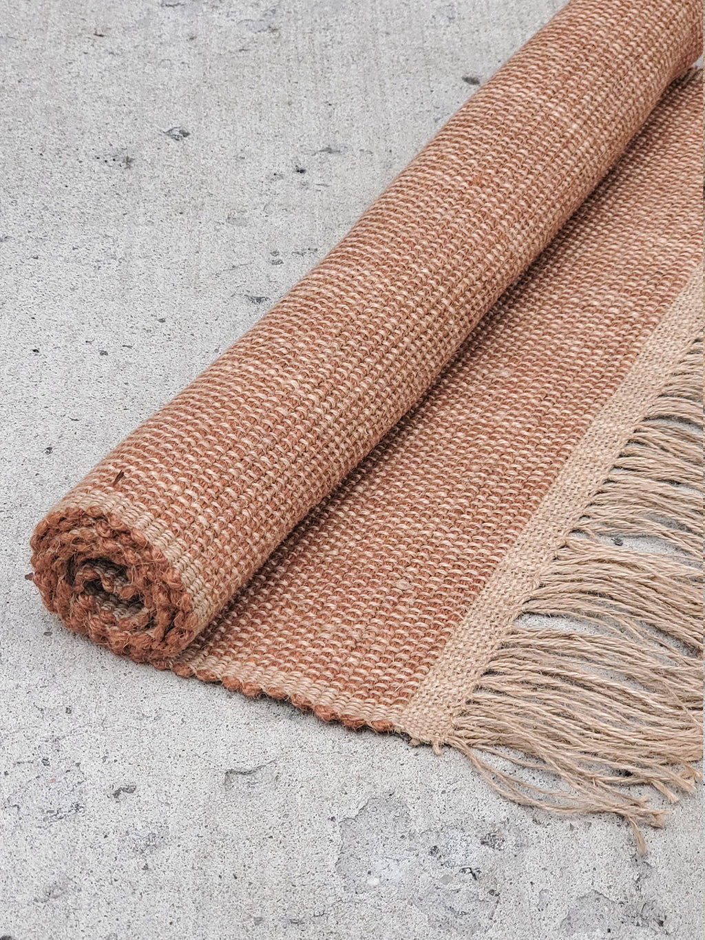 Rolled jute rug with fringes on a concrete surface
