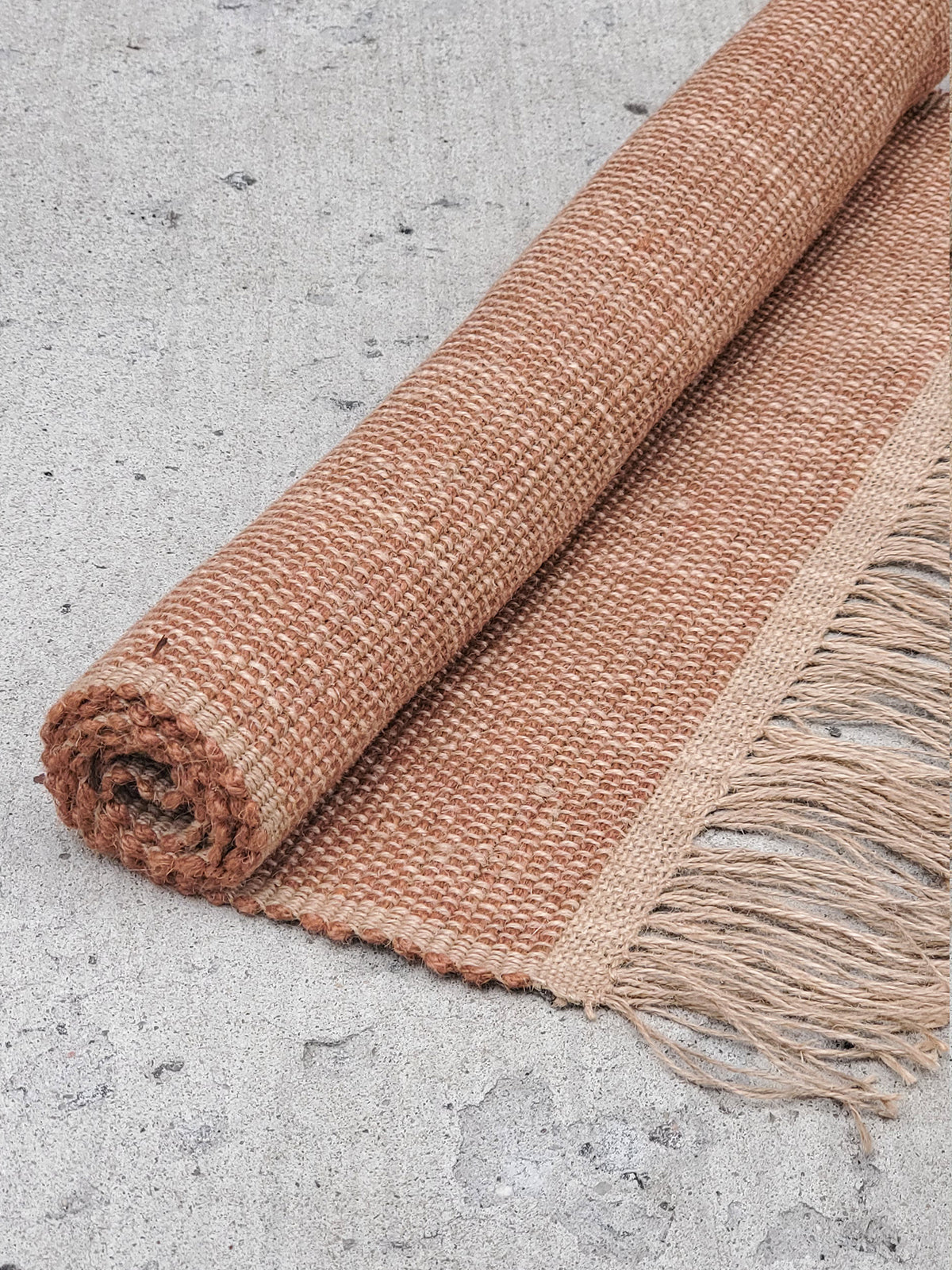 Rolled jute rug with fringes on a concrete surface
