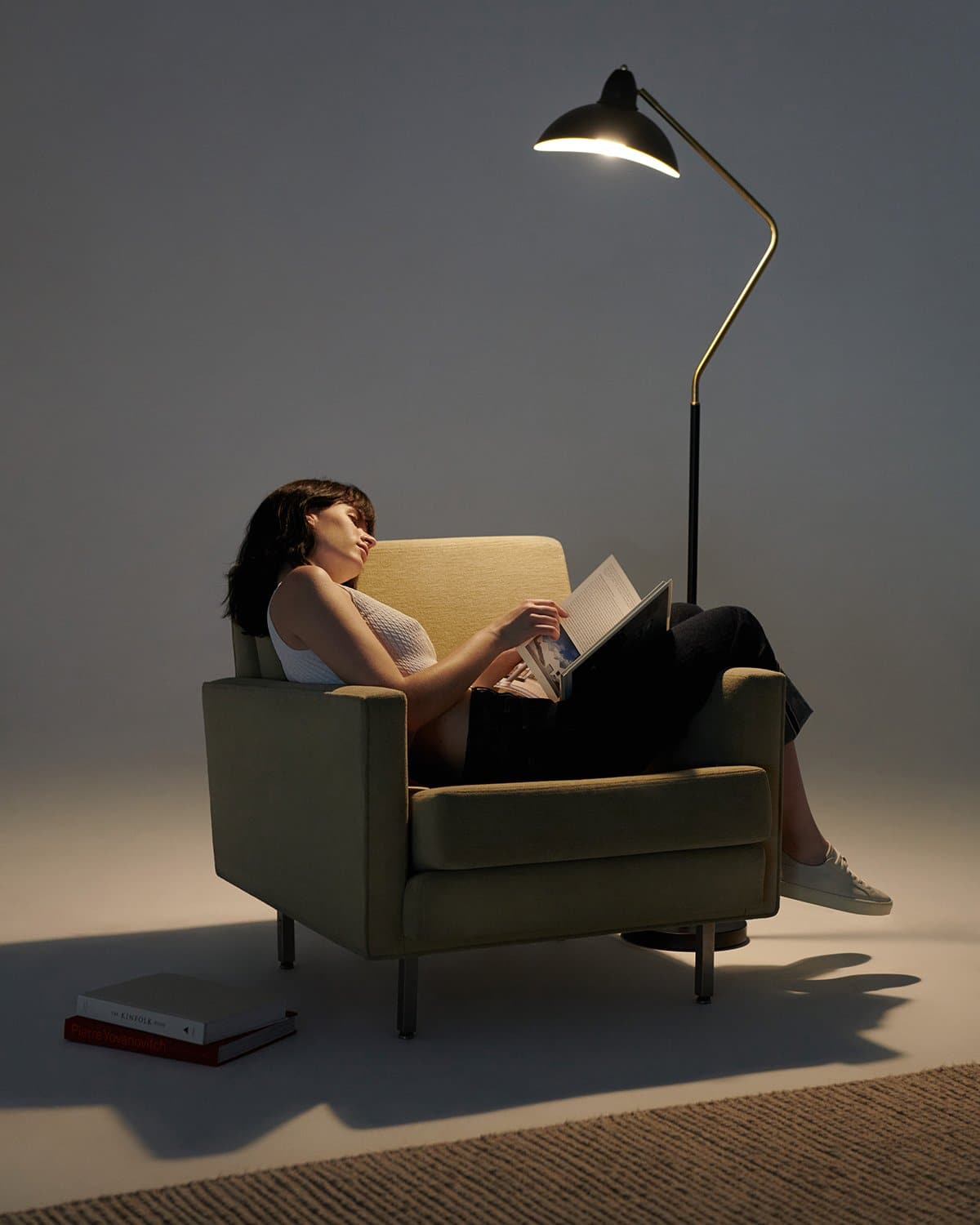 Woman reading a book in a dimly lit room with a floor lamp.