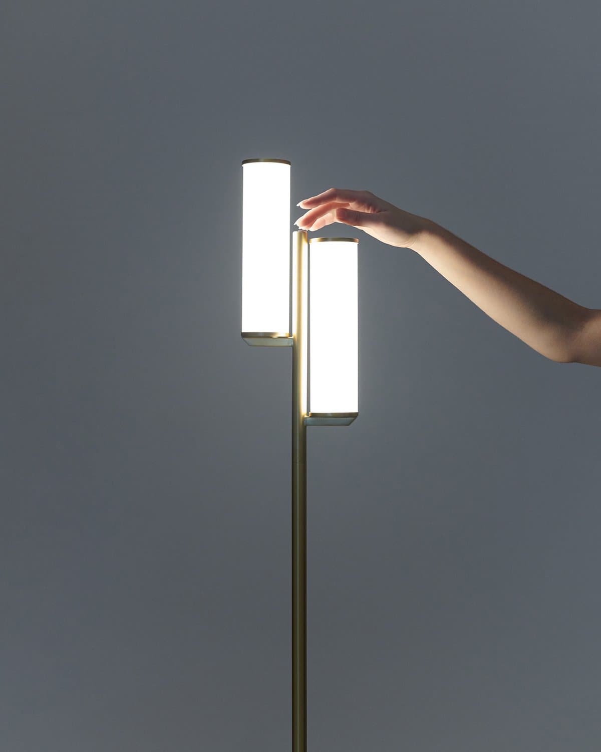 Modern floor lamp with a hand reaching out to touch it against a dark background