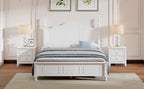 White bedroom set with bed, nightstands, and lamps in a room with framed artwork on the wall.
