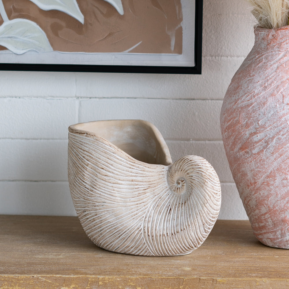 Decorative shell-shaped vase on a wooden surface with a framed abstract painting in the background.
