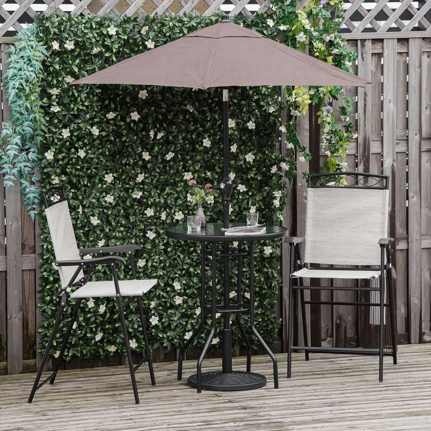 Outdoor patio set with table and chairs under a large umbrella against a green foliage wall.