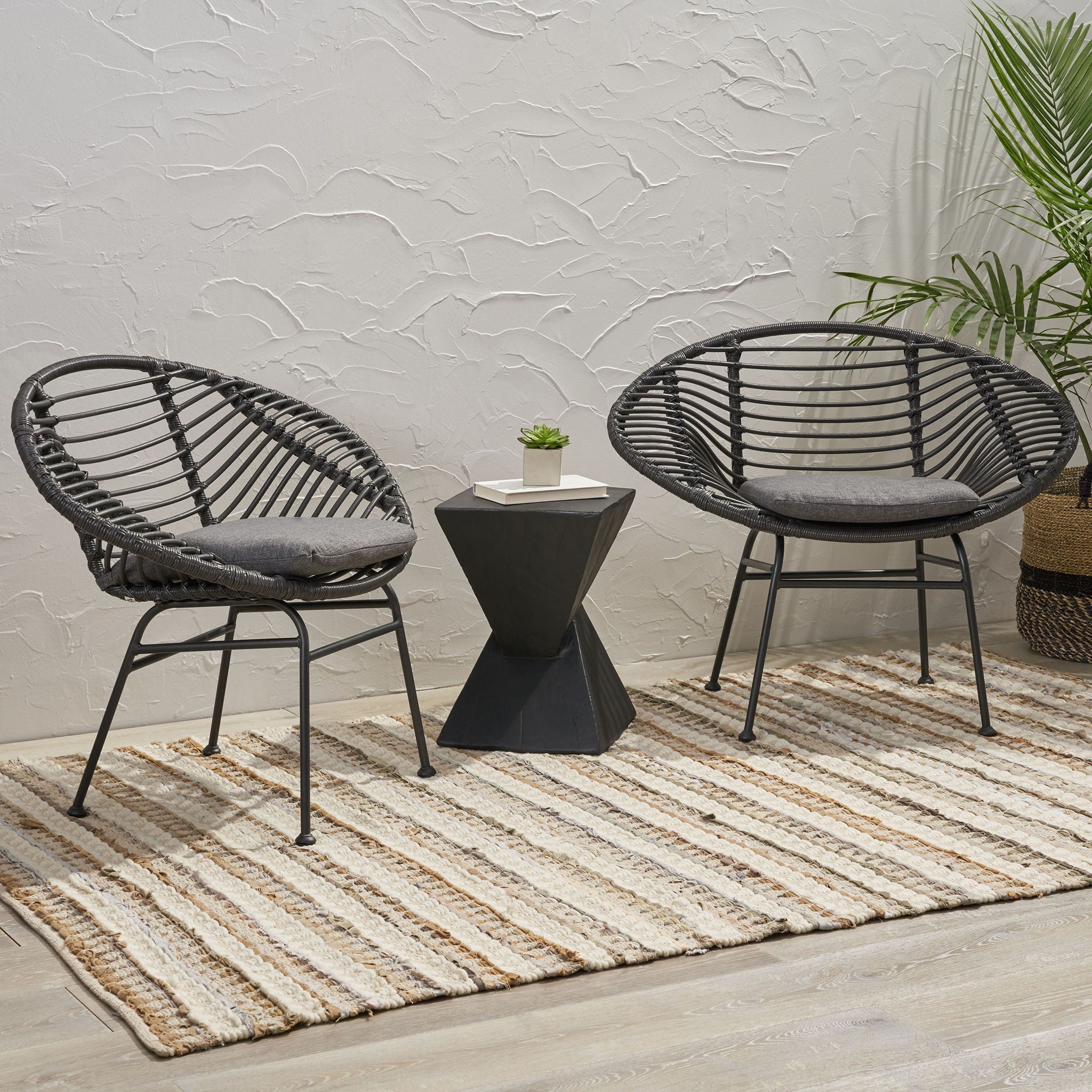 Two dark woven chairs with a small table on a striped rug against a textured wall.