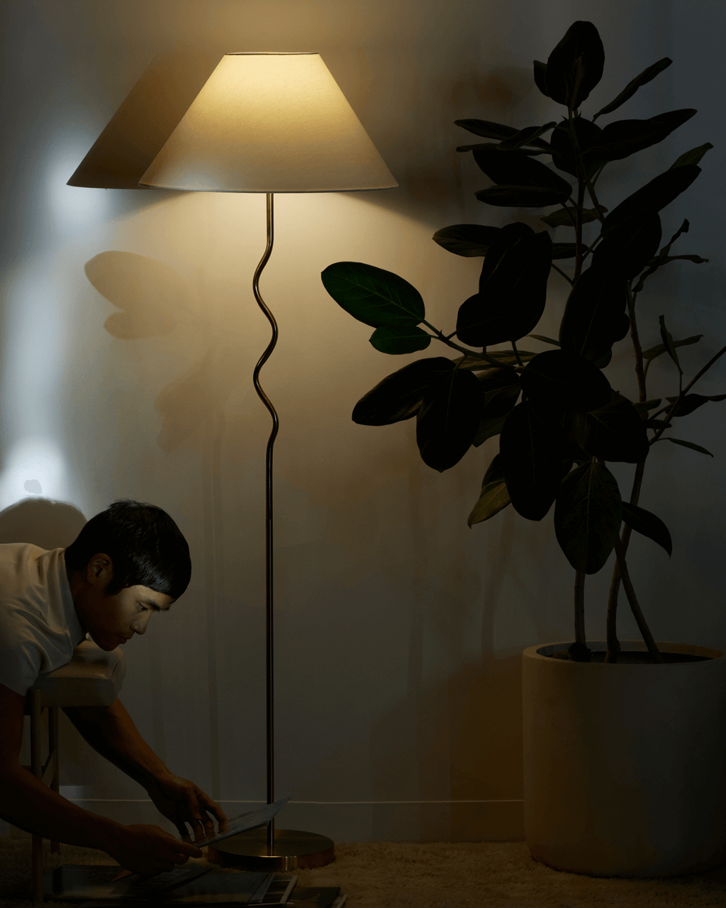 Person using a tablet in a dimly lit room with a floor lamp and plant.