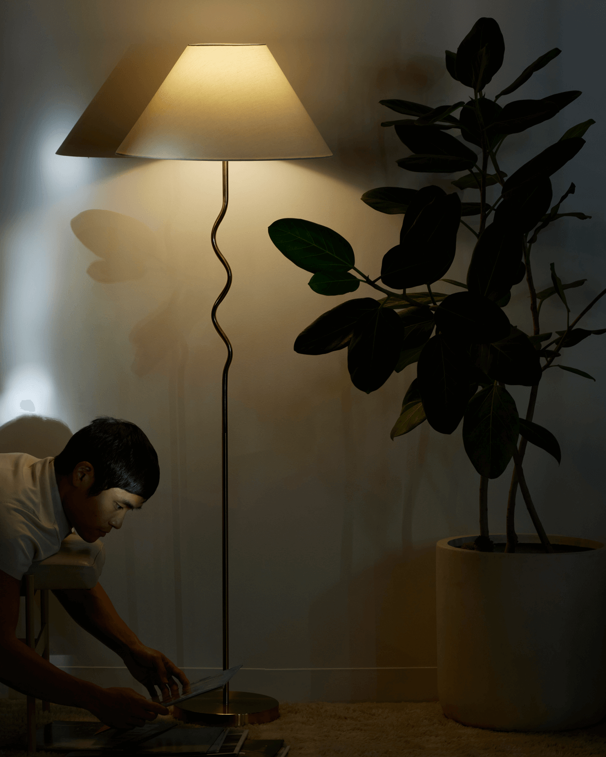 Person using a tablet in a dimly lit room with a floor lamp and plant.