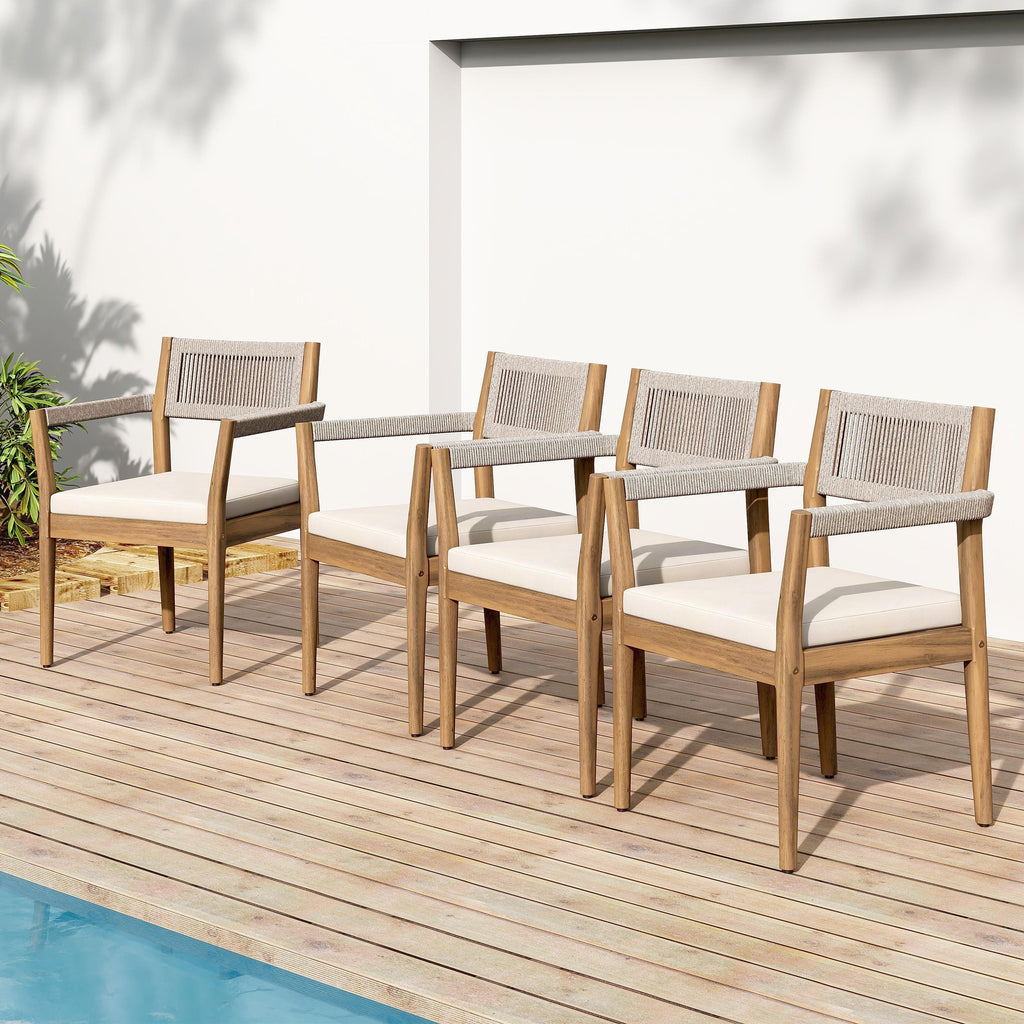 Set of four wooden chairs with white cushions on a wooden deck by a pool.