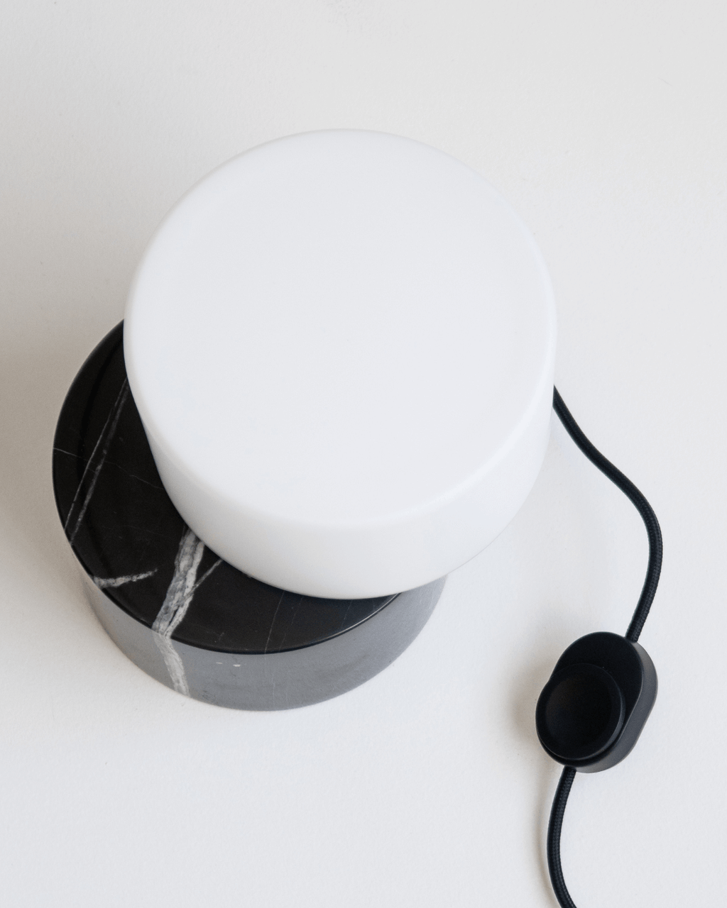 White spherical lamp with black marble base on a white surface