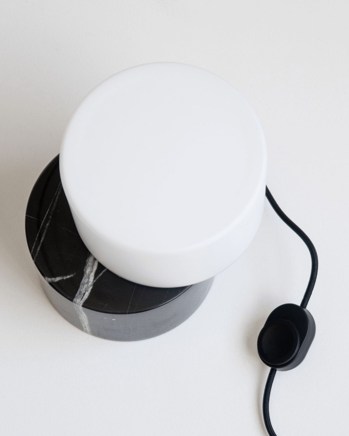 White spherical lamp with black marble base on a white surface