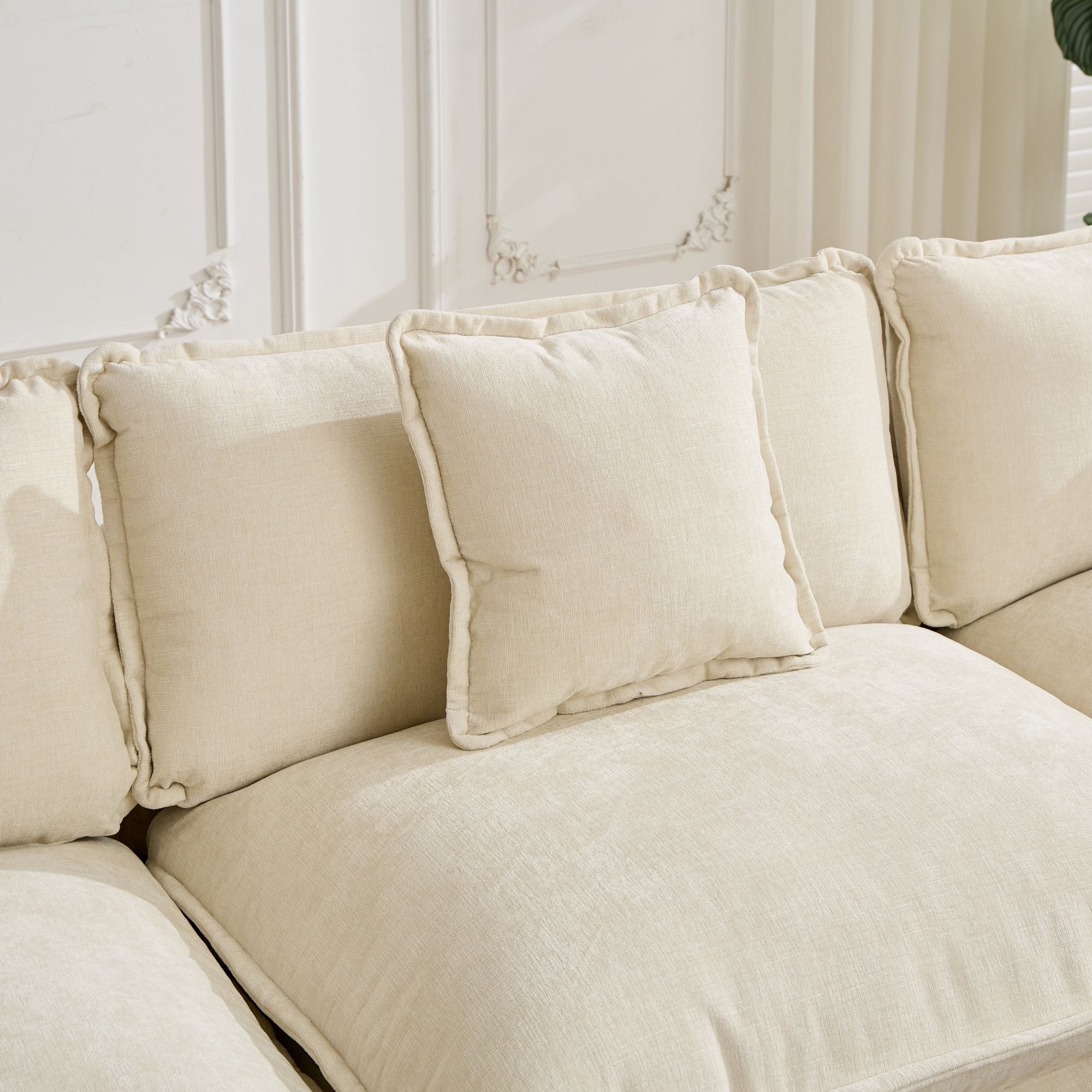 Beige sectional sofa with decorative pillows against a neutral wall.