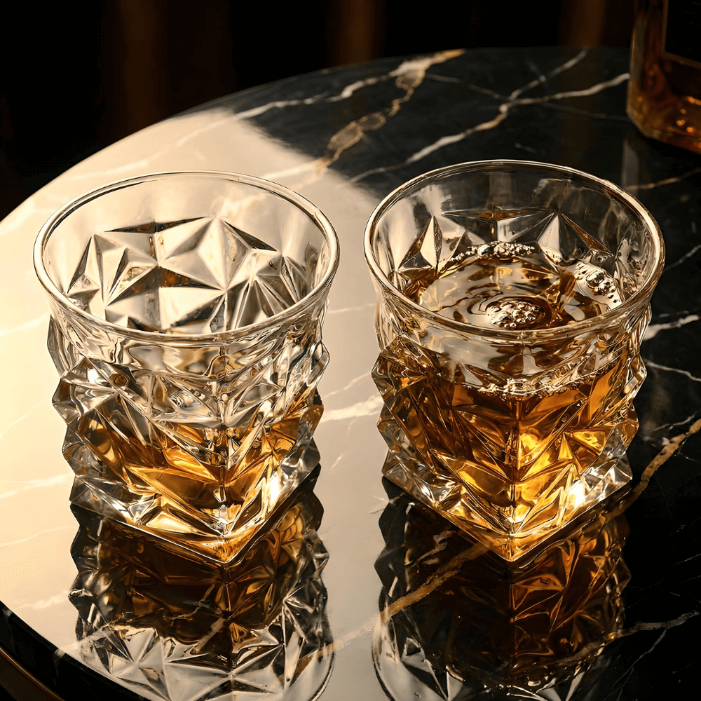 Two crystal glasses filled with whiskey on a reflective surface