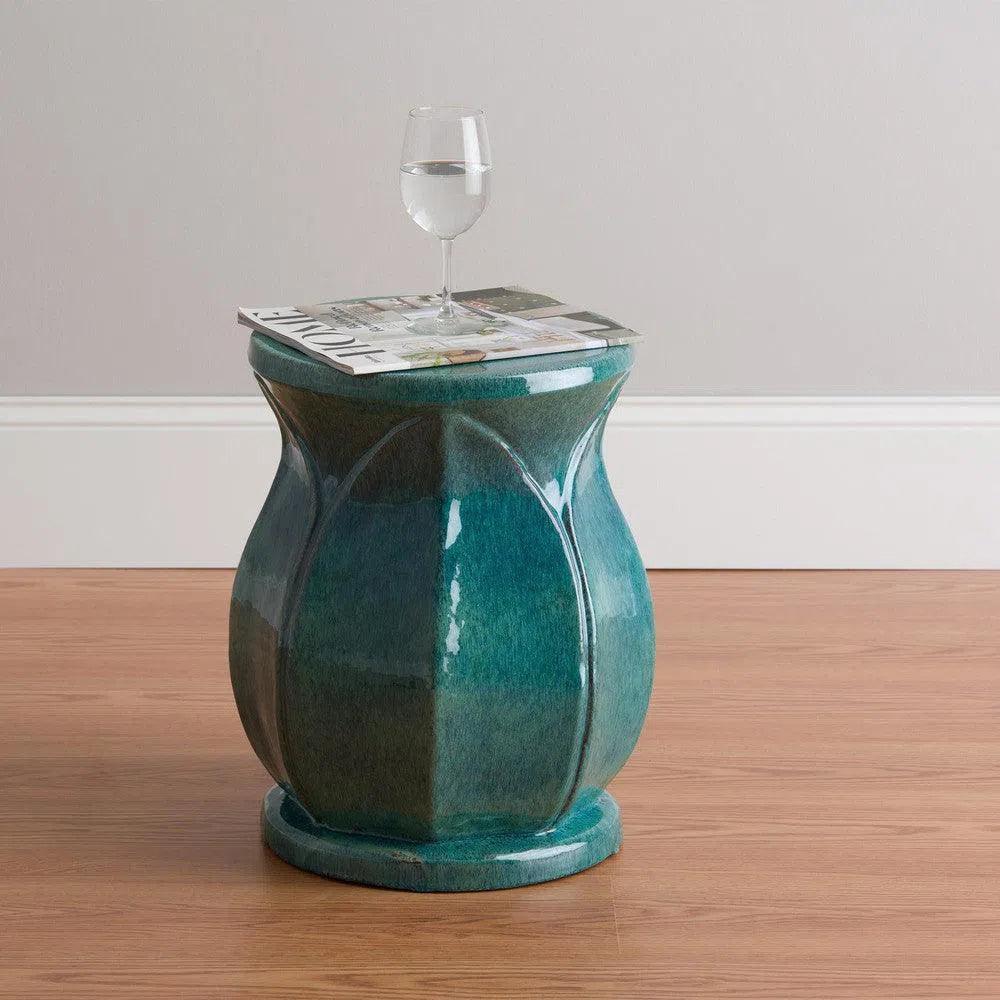 Teal ceramic side table with a glass of water on top, against a plain wall.