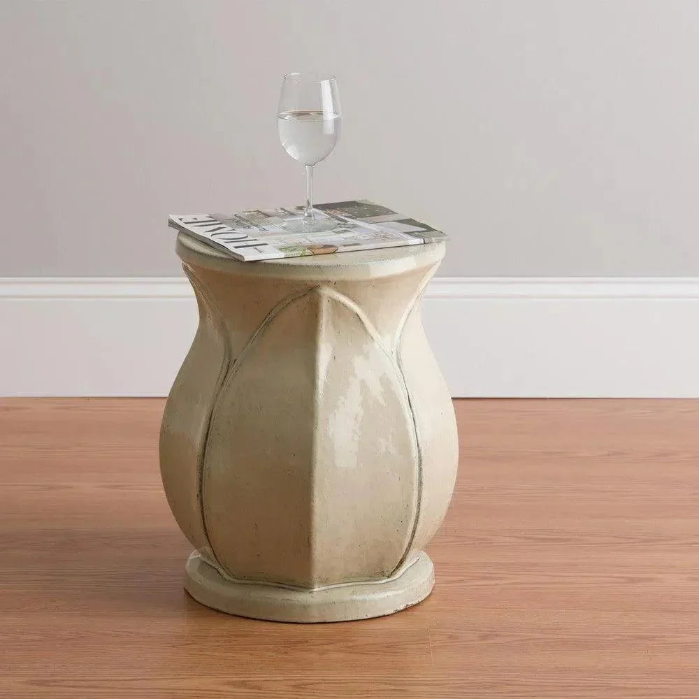 Decorative side table with a glass on top against a plain wall.