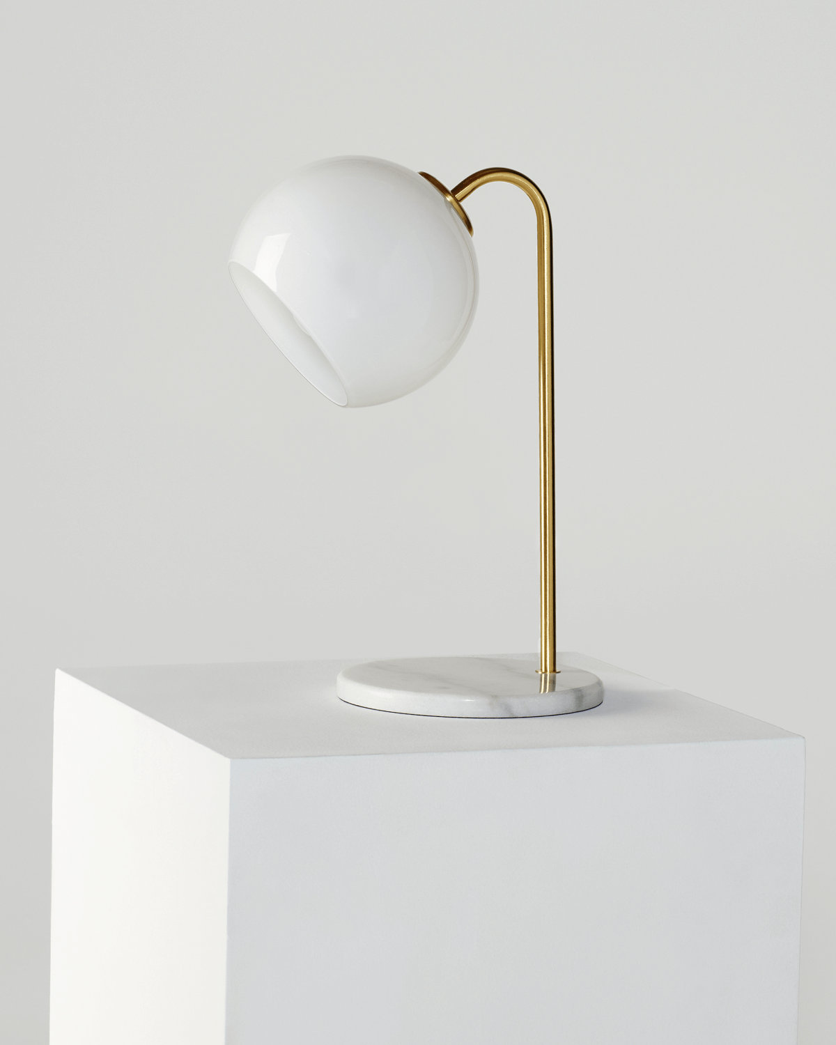 Table lamp with white shade and gold curved arm on a white surface
