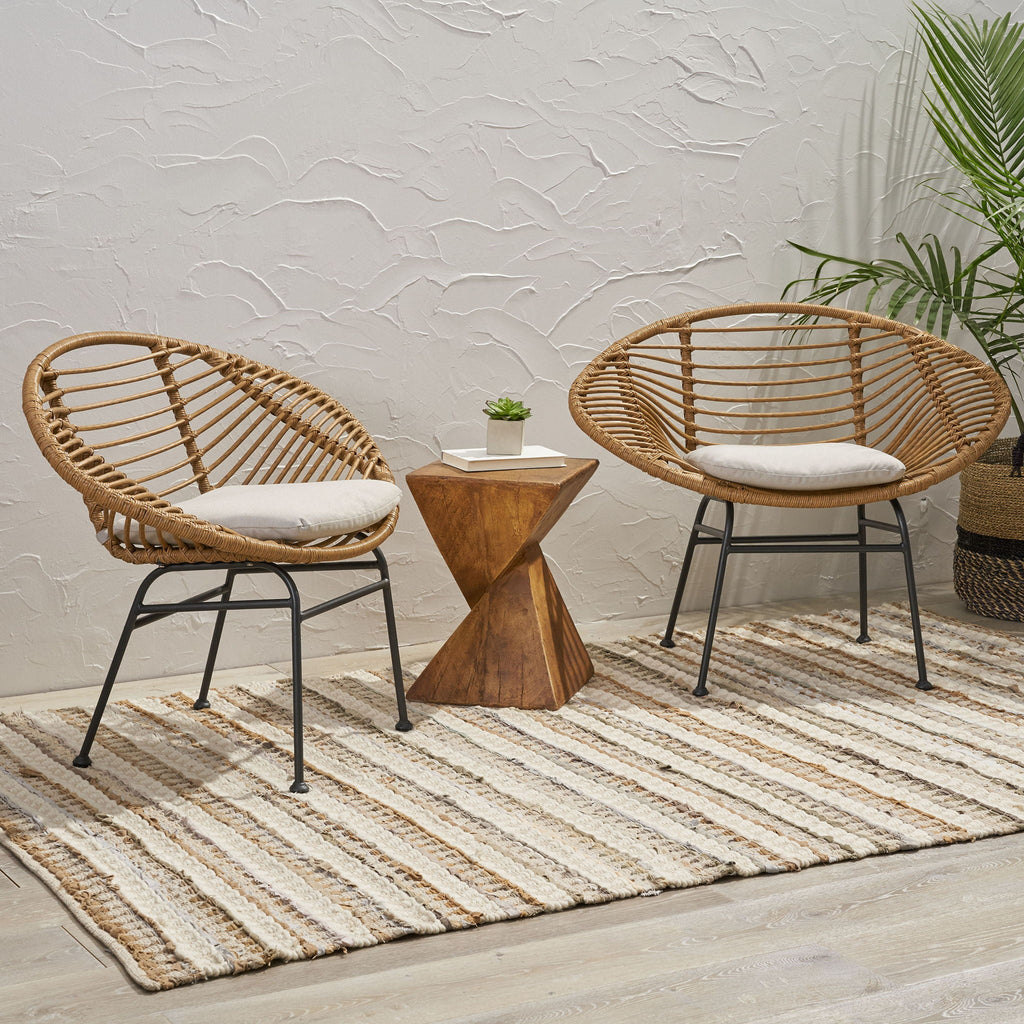 Two wicker chairs with cushioned seats and a small wooden table on a striped rug.