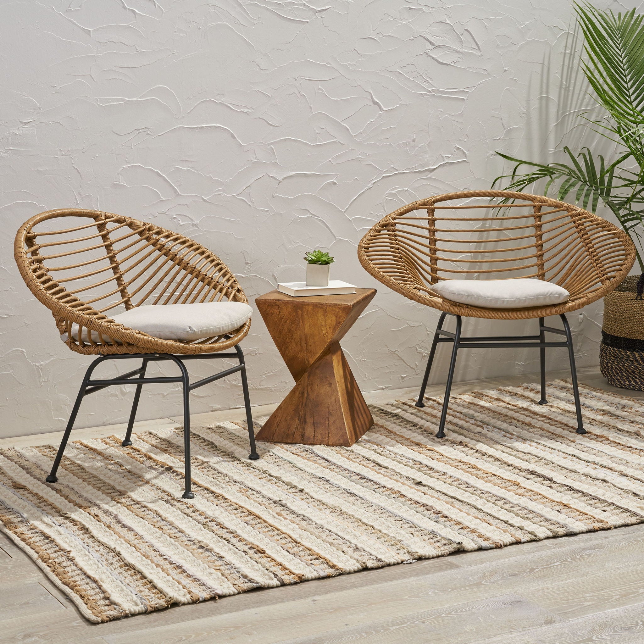 Two wicker chairs with cushioned seats and a small wooden table on a striped rug.