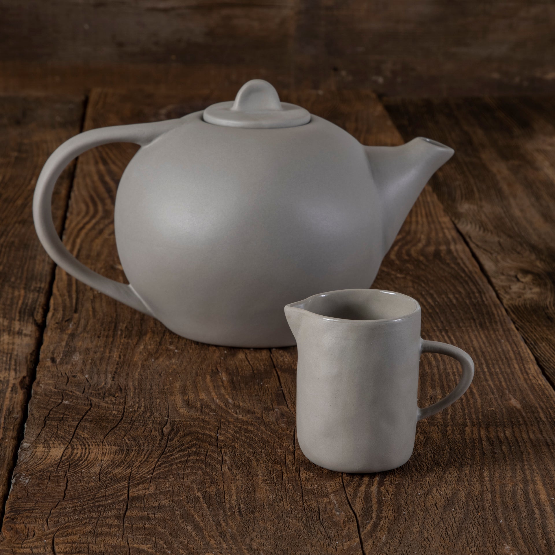 White ceramic teapot and small pitcher on a wooden surface
