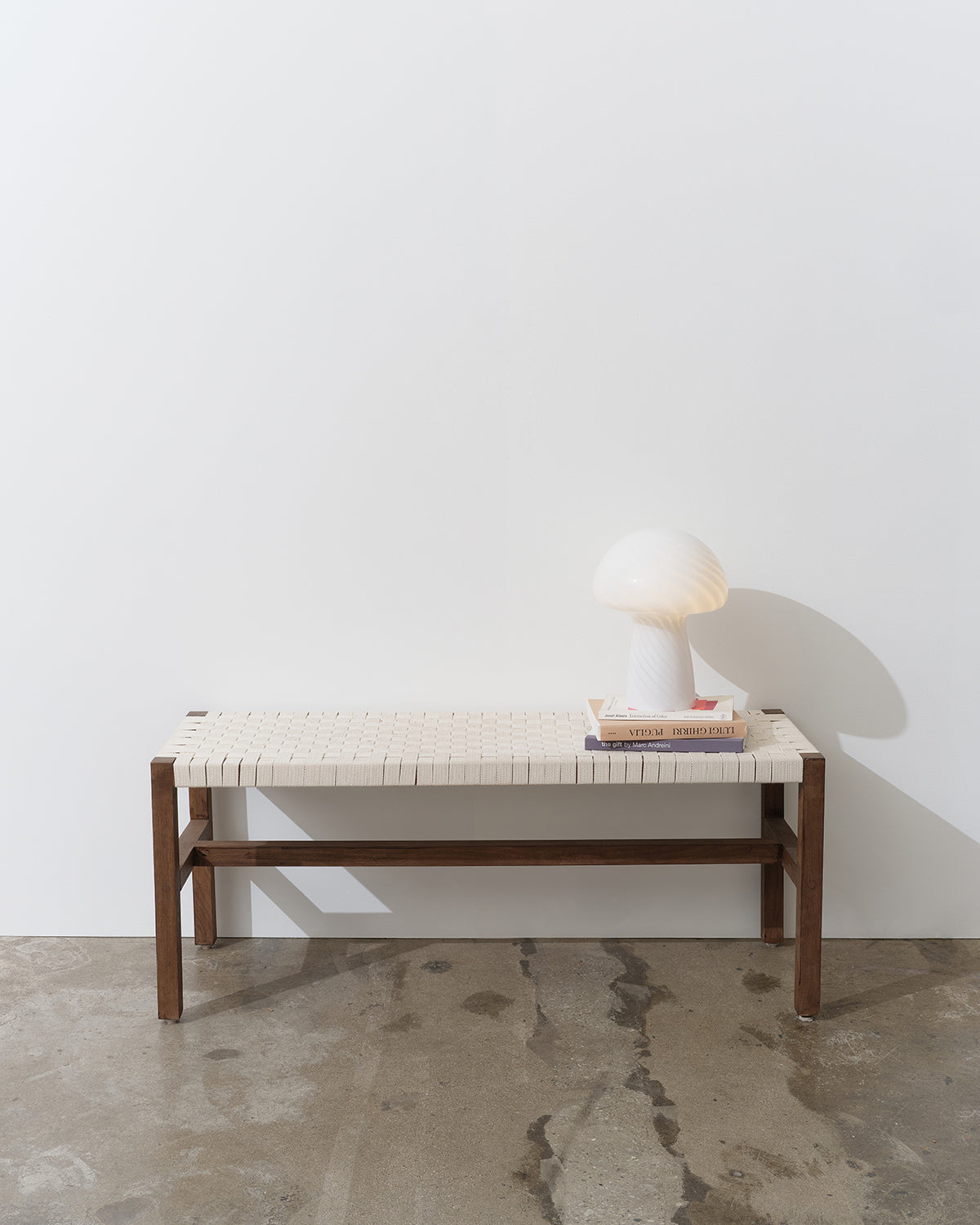 White lamp on a wooden bench with woven seat against a white wall