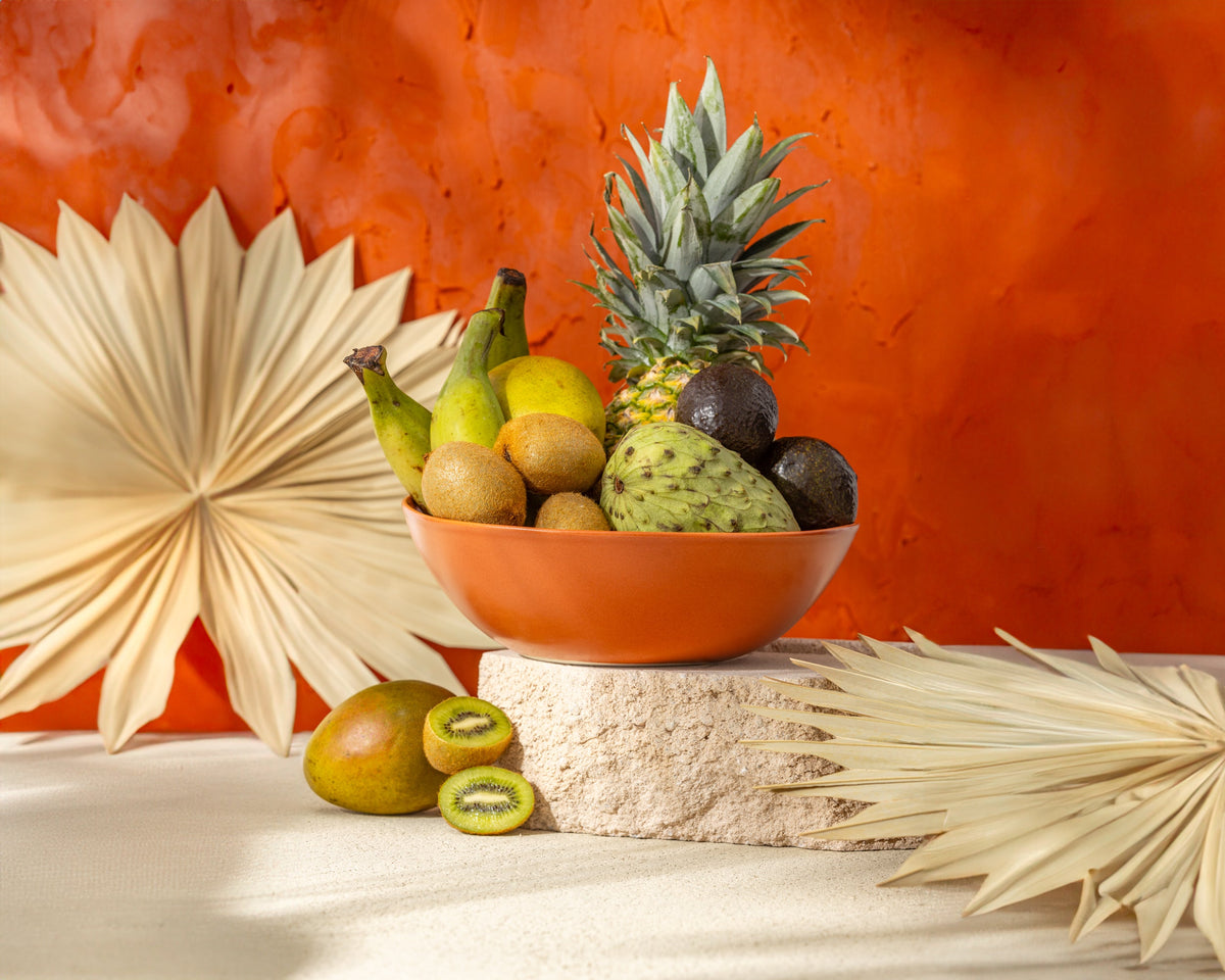 Fruit bowl with pineapple, bananas, and other fruits on a textured surface with an orange wall background.