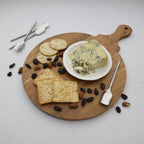 Wooden cutting board with blue cheese, crackers, and raisins on a white background