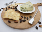 Wooden cutting board with blue cheese, crackers, and dried fruits on a white surface