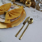 Gold cutlery set on a table with a yellow napkin and decorative plates.