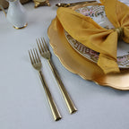 Gold cutlery set on a white tablecloth with a decorative plate and yellow napkin.