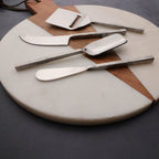 Set of metal cheese knives on a round stone and wood cutting board.