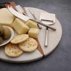 Cheese platter with cheese, crackers, and olive on a marble board with cheese knives.