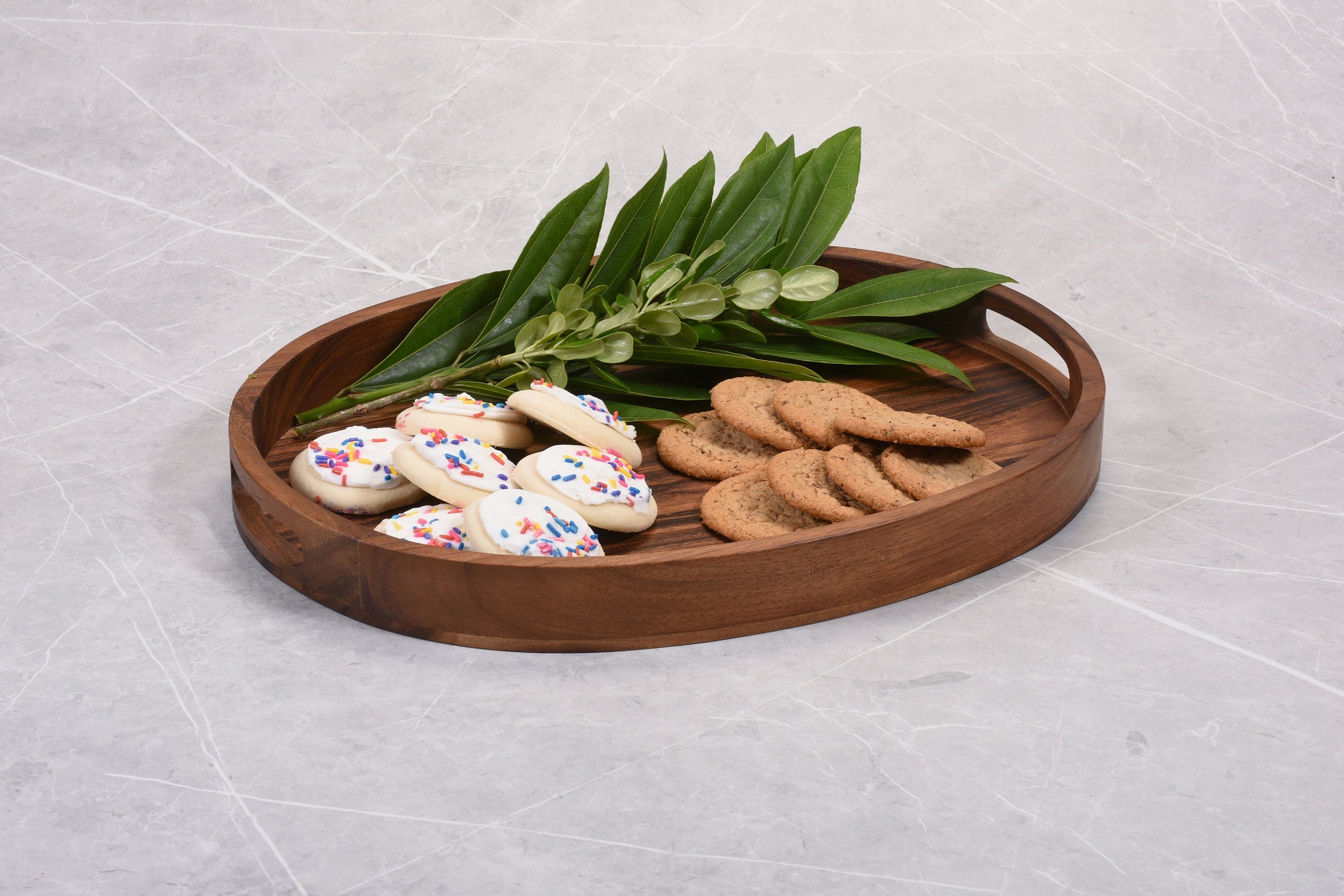 Wooden tray with cookies and green leaves on a light gray surface