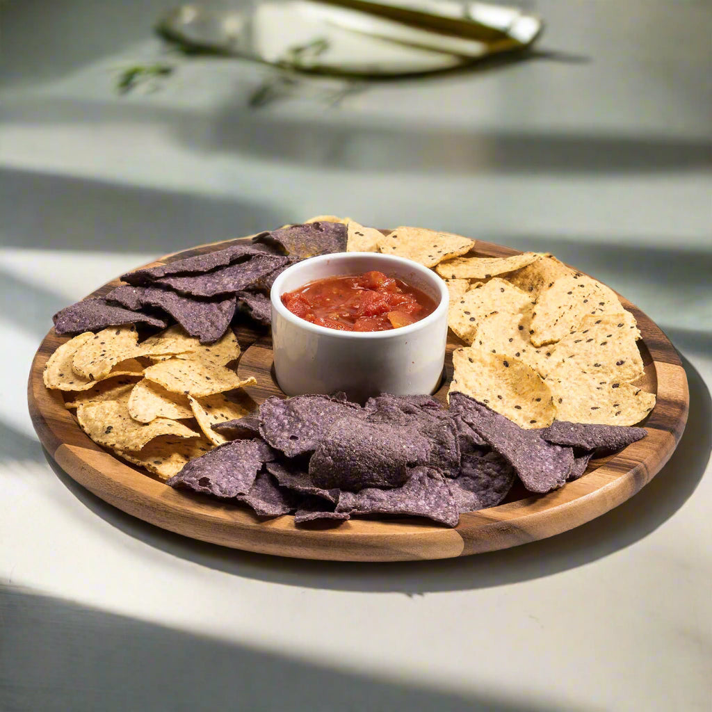 Wooden platter with tortilla chips and a bowl of salsa on a light surface.