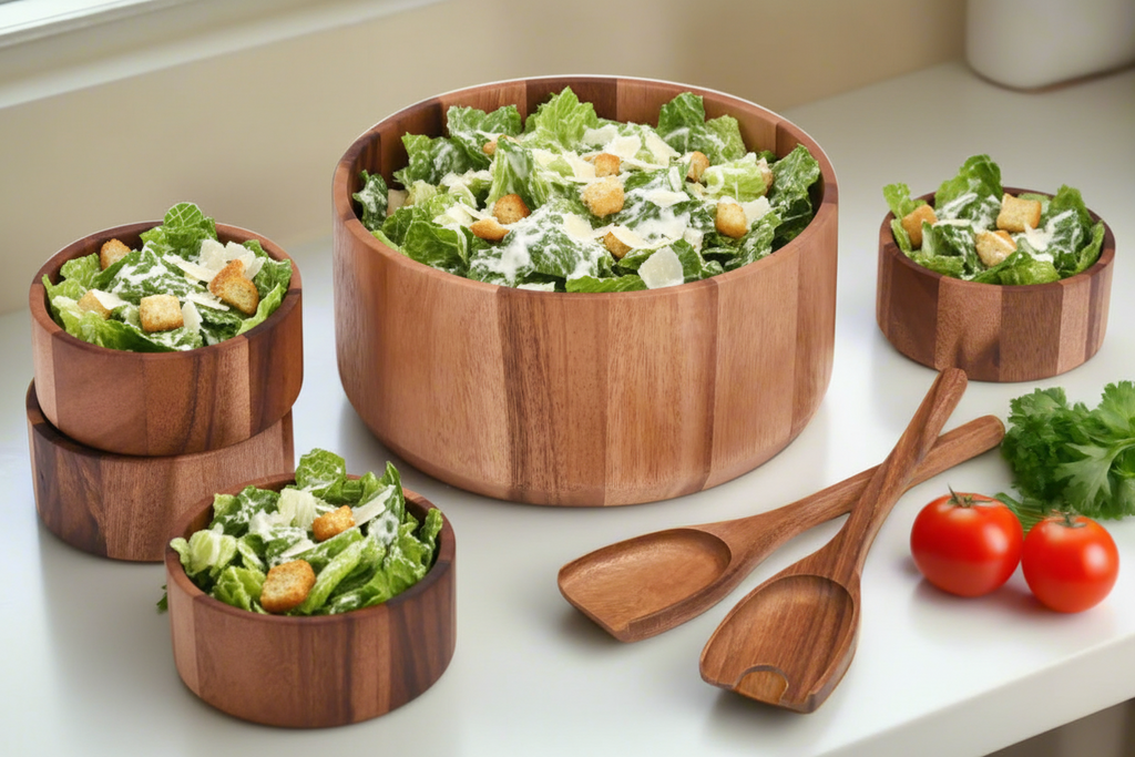 Wooden salad bowls with Caesar salad and wooden spoons on a white surface.