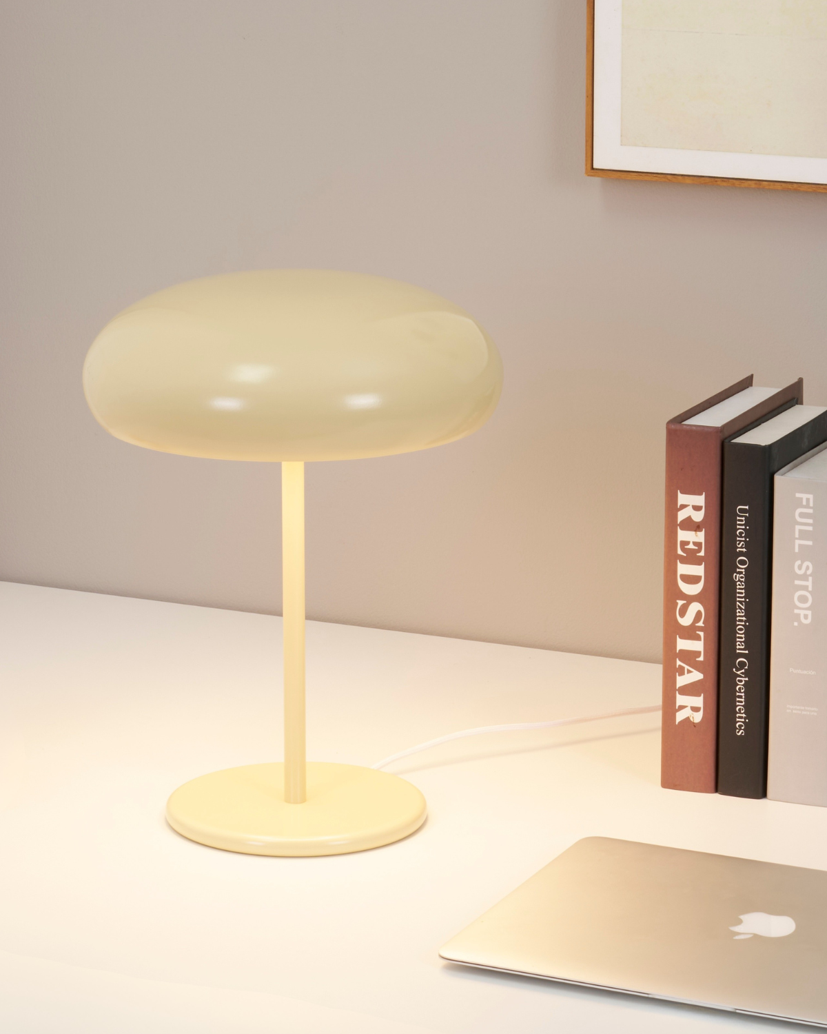 Modern table lamp on a desk with books and a laptop in the background