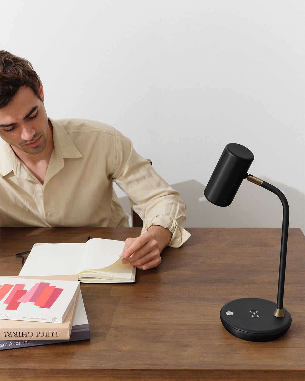 Man sitting at a desk with a black adjustable desk lamp, books, and a notebook.