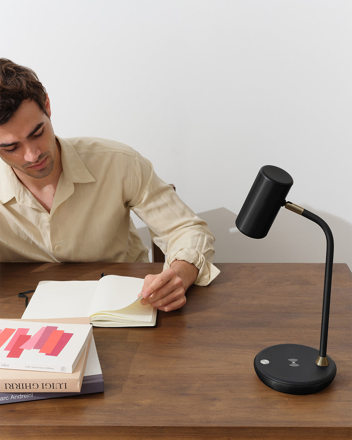 Man sitting at a desk with a black adjustable desk lamp, books, and a notebook.