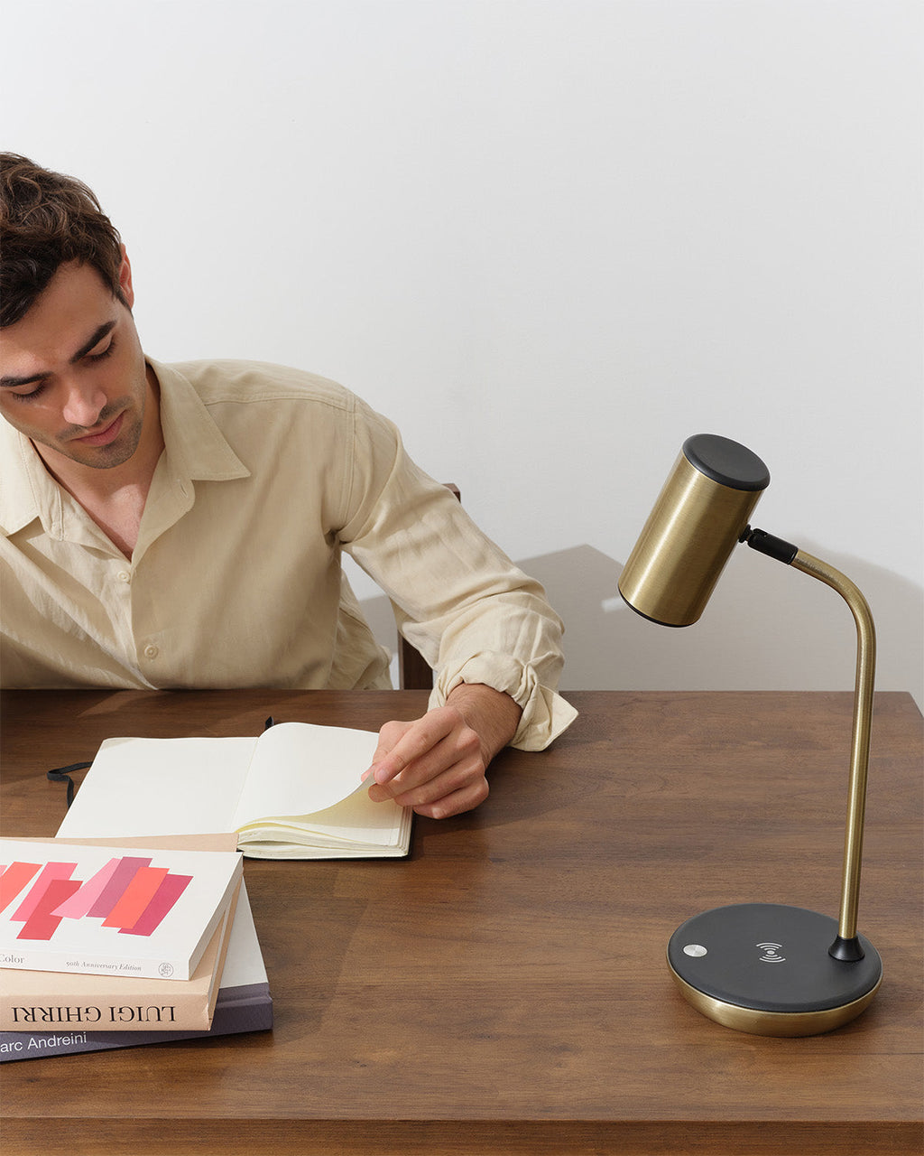 Man reading a book with a gold desk lamp on a wooden table