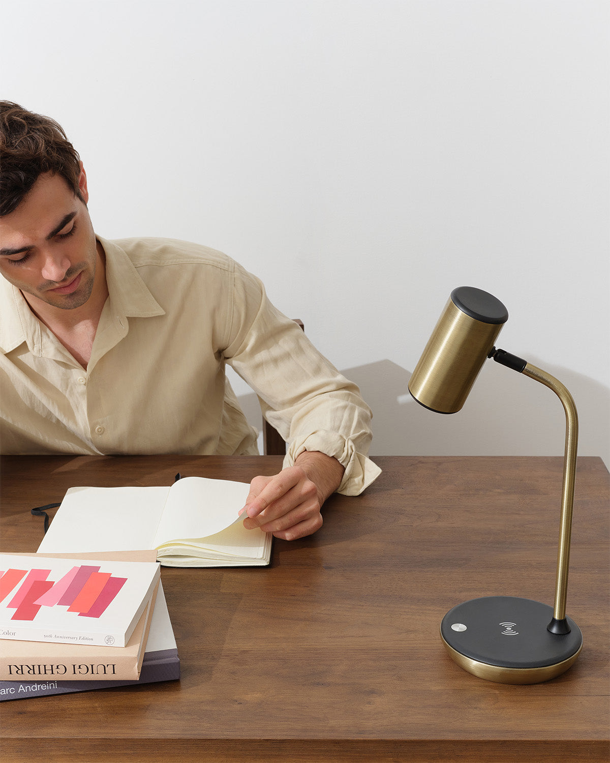 Man reading a book with a gold desk lamp on a wooden table
