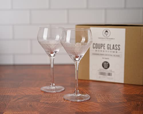 Two coupe glasses on a wooden surface with a box labeled 'Coupe Glass' in the background.