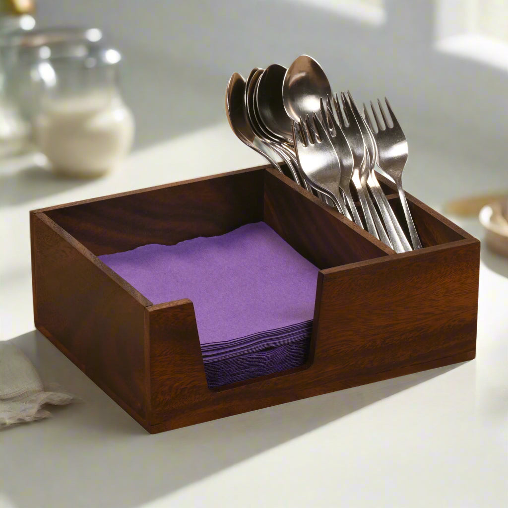 Wooden utensil holder with silverware and purple napkins on a light surface.