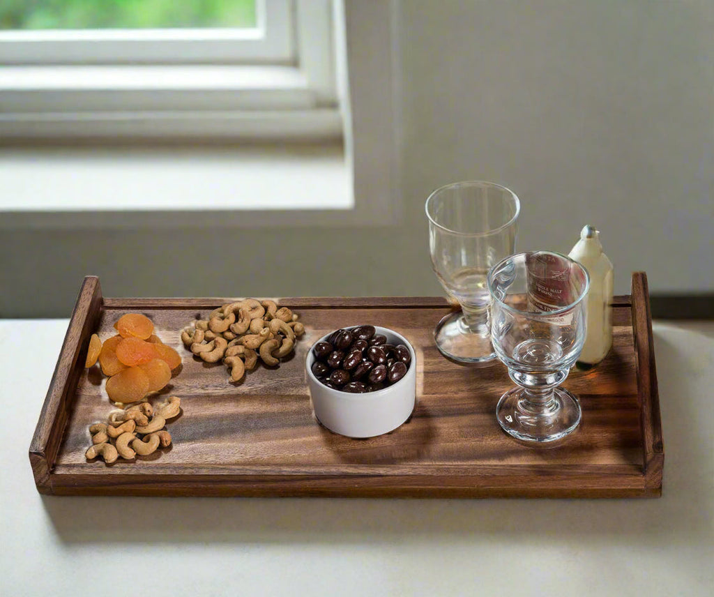 Wooden tray with snacks and drinks on a light surface near a window.