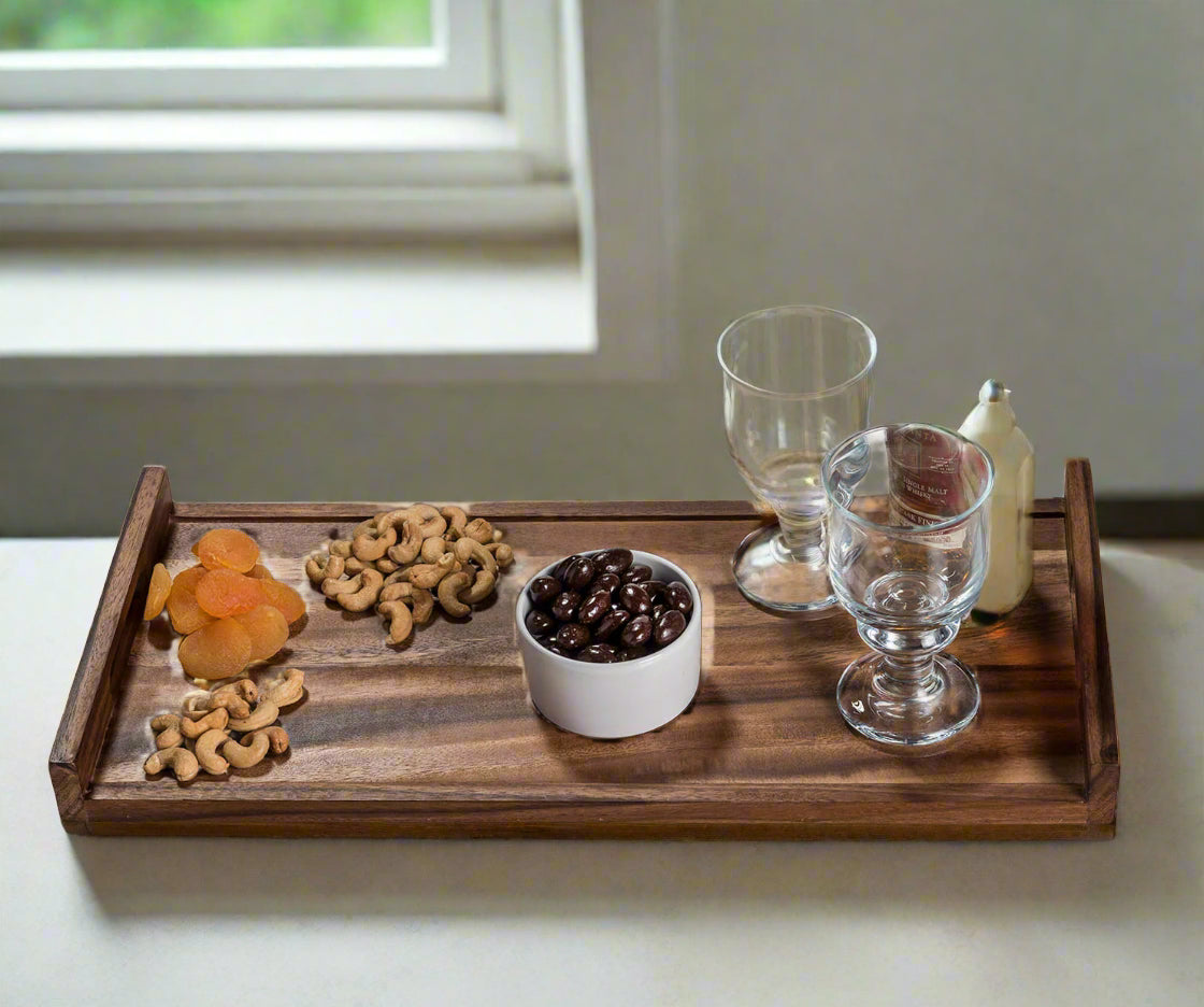 Wooden tray with snacks and drinks on a light surface near a window.
