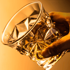 Hand holding a crystal glass with a warm glow on a yellow background